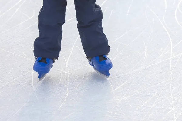 Benen van een man in blauwe schaatsen rijdt op een ijsbaan — Stockfoto