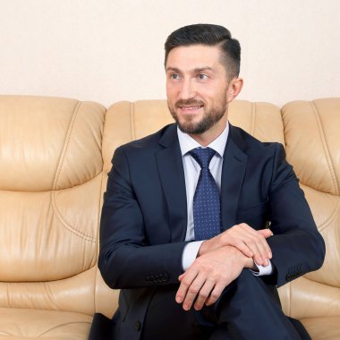 Gülümseyen başarılı bir iş adamı deri bir couc üzerinde oturuyor.