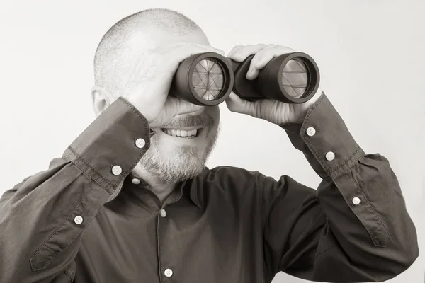 Uomo barbuto con binocolo in mano guardando felicemente in th — Foto Stock