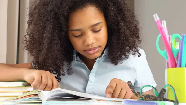 Colegial de pele escura lendo um livro fazendo lição de casa — Fotografia de Stock