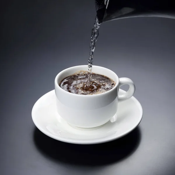煮えたぎる湯を黒コーヒーと一緒に白いカップに注ぐ。ホットd — ストック写真