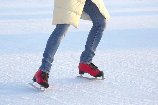Girl in blue jeans actively skates on red ice skates on an ice r — Stock Photo, Image