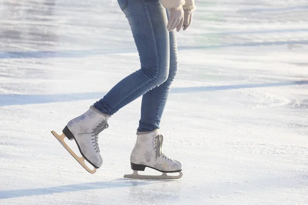 Mädchen in blauen Jeans Schlittschuhe auf weißen Schlittschuhen auf einer Eisbahn. Sport — Stockfoto