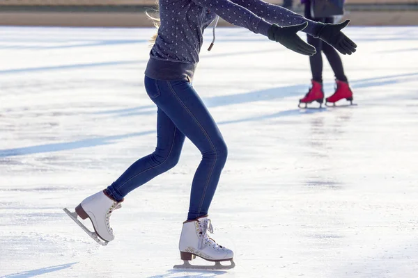 Gambe di una ragazza in jeans blu e pattini bianchi su una pista di pattinaggio su ghiaccio. ho — Foto Stock