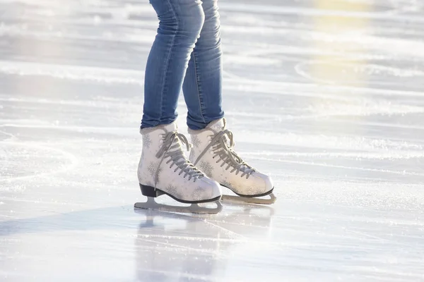 Pernas de uma menina em jeans azuis e patins brancos em uma pista de gelo. ho — Fotografia de Stock