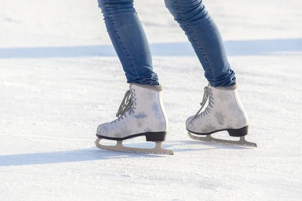 Pernas de uma menina em jeans azuis e patins brancos em uma pista de gelo. ho — Fotografia de Stock