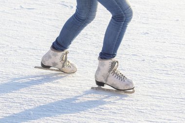 legs of a girl in blue jeans and white skates on an ice rink. ho