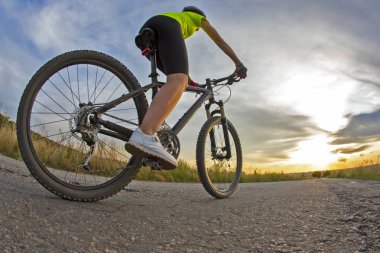 Güzel kız bisikletçi gün batımında yolda bisiklet sürüyor.