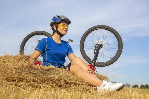 Schöne Radfahrerin sitzt auf trockenem Gras auf dem Hintergrund der — Stockfoto