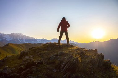 Elleri havada bir adam, gün doğumuna kadar dağın tepesinde duruyor. Dağlarda turist gezgini güneşli bir şafakla tanışır.