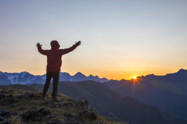 Elleri havada bir adam, gün doğumuna kadar dağın tepesinde duruyor. Dağlarda turist gezgini güneşli bir şafakla tanışır.