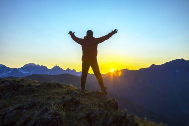 Elleri havada bir adam, gün doğumuna kadar dağın tepesinde duruyor. Dağlarda turist gezgini güneşli bir şafakla tanışır