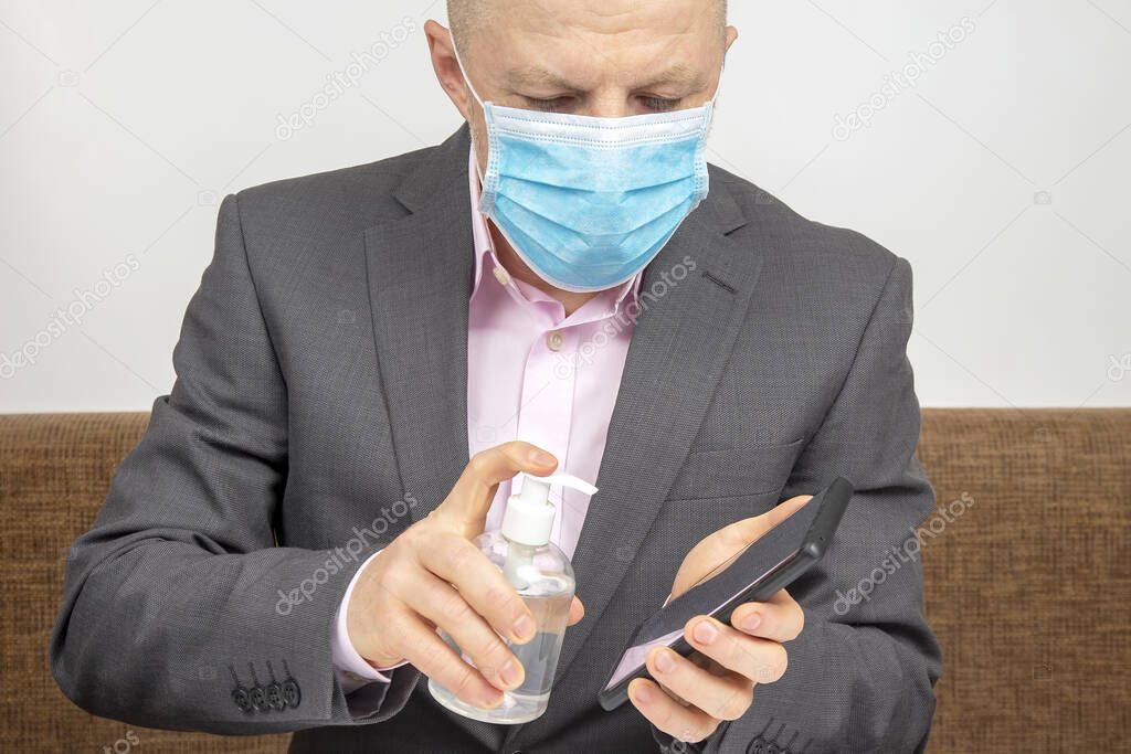 man at home in quarantine with a medical mask on his face disinfects a mobile smartphone with an alcohol solution from infection with the virus. Recommendations during the coronavirus epidemic.