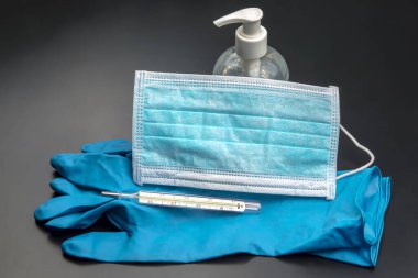Tıbbi maske, steril eldivenler, termometre ve siyah arka planda alkol dezenfektanı. Koronavirüse karşı pandemik ve koruyucu öğeler