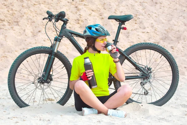漂亮的女自行车手从热水瓶里倒茶在沙滩上的自行车的背景上 体育和娱乐 业余爱好和健康 自然与人类 — 图库照片
