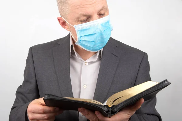 man in a business suit with a medical mask on his face is studying the bible.