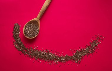 Kırmızı arka planda gülümseme şeklinde dağınık chia tohumları olan ahşap kaşık.