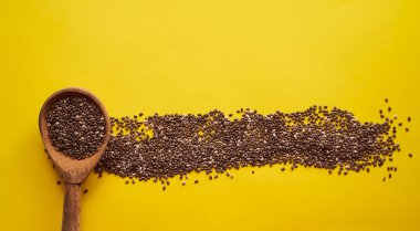 Sarı arka planda dağınık chia tohumlu ahşap kaşık var. Pankart