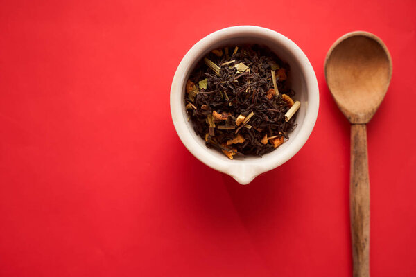 tea leaves with slices of fruit in a white bowl and a wooden spoon on a red background/top view