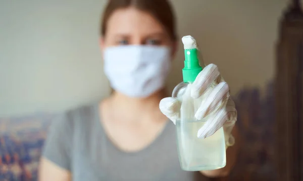 Elinde antiseptik olan koruyucu maskeli ve eldivenli bir kız.