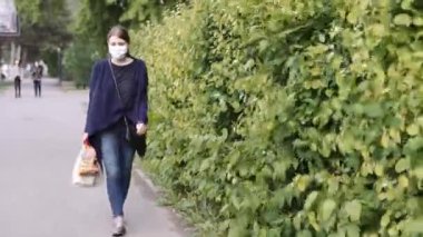 Beyaz tıbbi maskeli bir kız kasabada market alışverişiyle dolaşıyor. Çok kaliteli görüntüler.