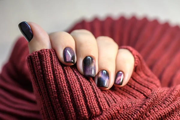 Beautiful nail polish in hand, purple nail art manicure, red background.