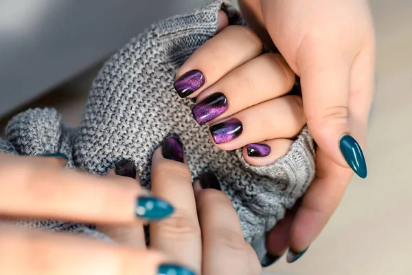 Beautiful nail polish in hand, purple nail art manicure, gray background.