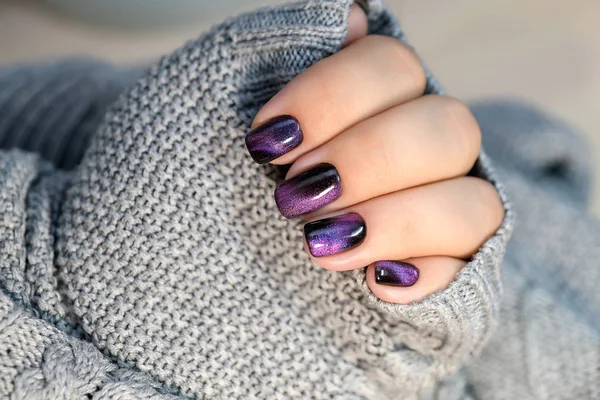 Beautiful nail polish in hand, purple nail art manicure, gray background.