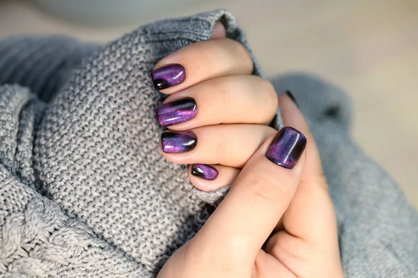 Beautiful nail polish in hand, purple nail art manicure, gray background.