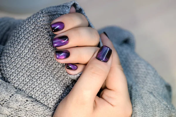 Hermoso esmalte de uñas en la mano, manicura de uñas de color púrpura, fondo gris Imagen de stock