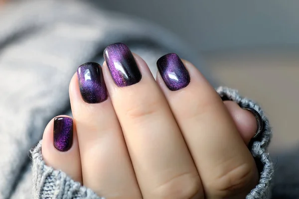 Hermoso esmalte de uñas en la mano, manicura de uñas de color púrpura, fondo gris Imagen de archivo