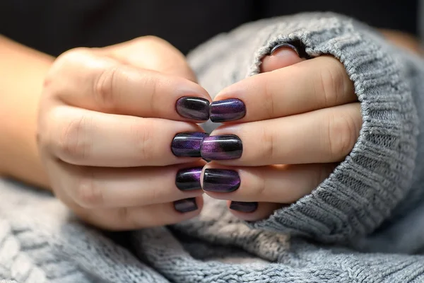 Hermoso esmalte de uñas en la mano, manicura de uñas de color púrpura, fondo gris Imágenes de stock libres de derechos