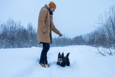 Adam kış ormanında köpeğiyle yürüyor.