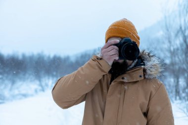 Kış ormanında sakallı bir adam fotoğraf çekiyor.