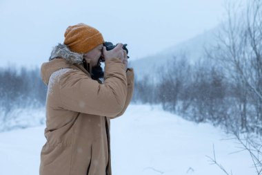 Kış ormanında sakallı bir adam fotoğraf çekiyor.
