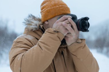 Kış ormanında sakallı bir adam fotoğraf çekiyor.