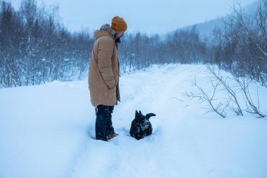 Adam kış ormanında köpeğiyle yürüyor.