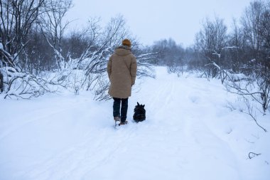 Adam kış ormanında köpeğiyle yürüyor.