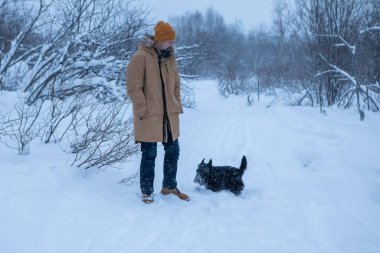 Adam kış ormanında köpeğiyle yürüyor.