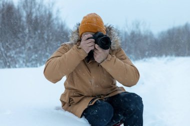 Kış ormanında sakallı bir adam fotoğraf çekiyor.