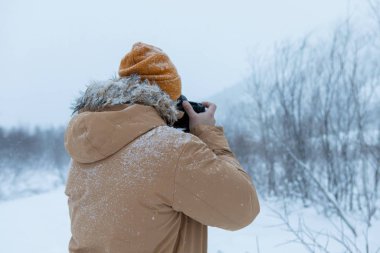 Kış ormanında sakallı bir adam fotoğraf çekiyor.
