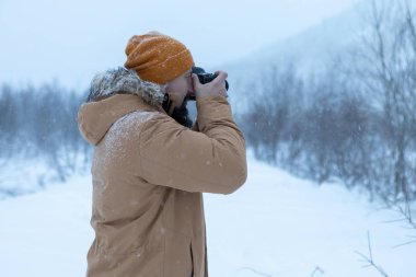 Kış ormanında sakallı bir adam fotoğraf çekiyor.