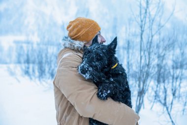 Bir adam köpeğini karda, sokakta tutuyor.