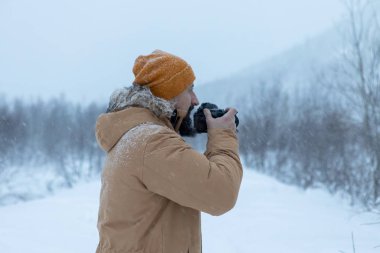 Kış ormanında sakallı bir adam fotoğraf çekiyor.