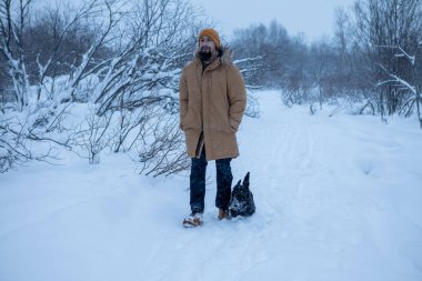 Adam kış ormanında köpeğiyle yürüyor.