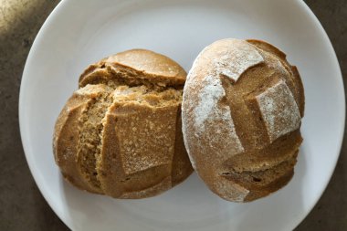 İki yumuşak taze pişmiş beyaz ekmek ve beyaz bir tabakta çıtır çıtır ekmek.