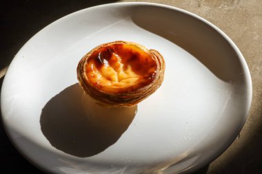 Dört Portekiz pastası, beyaz tabakta krema ve dokulu arka plan.