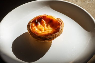 Dört Portekiz pastası, beyaz tabakta krema ve dokulu arka plan.