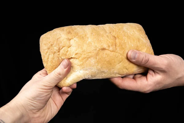 Man is sharing fresh bread ciabatta on black background. Two hands. — Stock Photo, Image