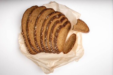 Çavdar ekmeği beyaz arka planda, ekmek kağıdının üzerinde parçalanmış olarak duruyor.